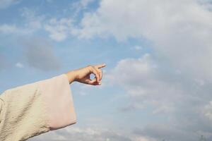 Hand reaching towards a bright blue sky with clouds photo