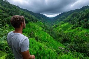 Man gazes over lush rice terraces under a dramatic sky in a moun photo