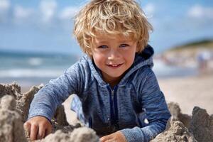 Boy builds sandcastle on sunny beach with clear sky and gentle w photo