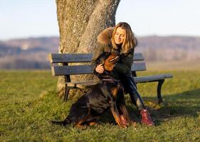 A woman sits on a bench and hugs a Rottweiler on a hill in the morningWoman sitting hugging Rottweiler on hill morning photo