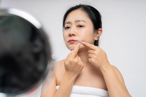 Asian woman popping pimples on her face in front of the mirror photo