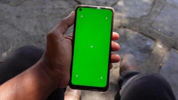 Hand holding smartphone with green screen displayed video