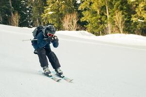 Close up freeze motion skier wearing helmet goggles carving on downhill snowy slope pine forest background fast winter sport action concept photo