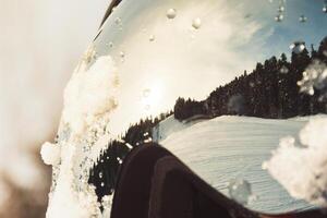 Macro view ski resort reflected in ski goggles with water drops, pine forest under clear winter sky, concept extreme sport, safety, perspective. photo