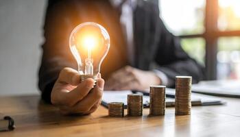 Businessman holds a glowing light bulb over growing stacks of coins. Business concept of innovation, investment, financial growth, energy saving, and money-making ideas. photo