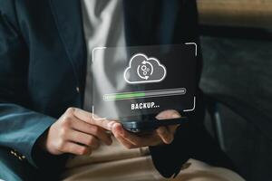 A business professional holds a smartphone displaying a digital backup cloud icon, symbolizing data security and technology. photo