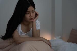 asian woman in bed late trying to sleep suffering insomnia, sleepless or scared in a nightmare, looking sad worried and stressed. Tired and headache or migraine waking up in the middle of the night photo