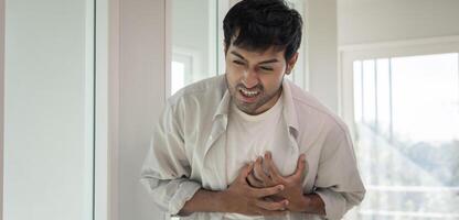 hold chest with heart attack symptoms. asian man have chest pain caused by heart disease, leak, dilatation, enlarged coronary heart, press on the chest with a painful expression photo