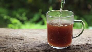 pouring hot water into a clear herbal tea cup on rustic wood with green background. concept of freshness, ancient herbs, health, relaxation, and herbal drink promotion video