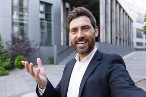 A businessman in a call, smiling and gesturing outdoors in front of a building photo