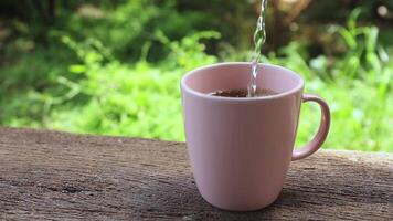pouring hot water into black coffee into pink cup with foam bubbles, coffee cup on wooden table in the morning in the garden, evoking freshness, warmth, and energy, ideal for cafe lifestyle video