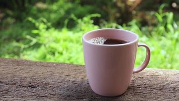 pouring sugar into black coffee in a pink cup on rustic wood with green background. concept of sugar consumption, diabetes risk, and health awareness video
