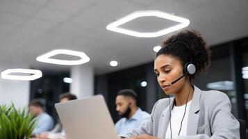 African American woman customer service agent with headset working on laptop in modern call center office. Professional support representative providing client assistance. photo