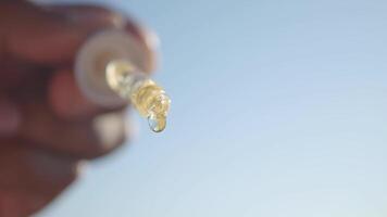 Hand holding dropper with liquid against clear sky video