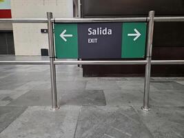 Exit sign with arrows to the right and left and translation into English and Spanish at the station. Emergency exit sign with bilingual directions in modern commercial space photo