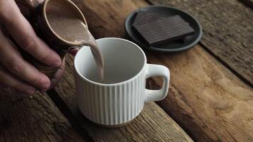 Cocoa or hot chocolate pouring into mug on rustic wooden background video