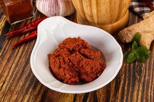 A bowl of red curry with spices and a wooden spoon photo