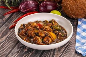 A bowl of food on a table with some vegetables and a coconut photo