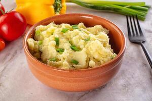 A bowl of mashed potatoes with vegetables on a table photo
