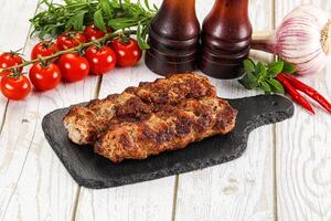 Two meat skewers on a black board with tomatoes and spices photo