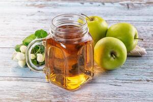 A jar of apple cider and some apples on a wooden table photo