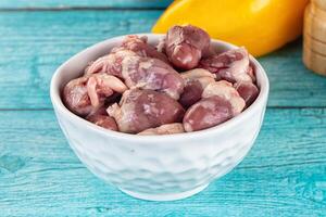 A bowl filled with raw chicken and a lemon photo