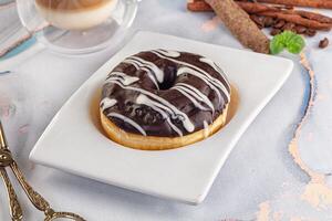 A chocolate donut with a white glaze on a white plate photo
