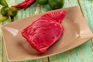 A piece of raw tuna on a plate with lime and green peppers photo