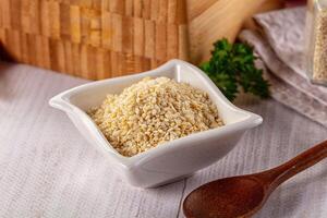 A bowl of sesame seeds and a wooden spoon on a table photo