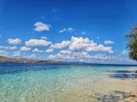 Serene Tropical Beach with Clear Water, Blue Sky and Fluffy Clouds photo