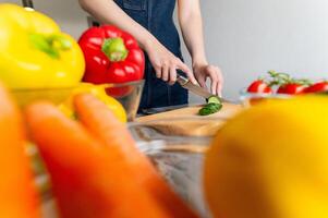 Hands cutting cucumber on wooden board. Woman in casual clothes cutting fresh vegetables. Preparing food photo