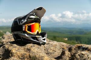 Side view of a full face black and white downhill mountain bike helmet. Extreme sports gear, against a backdrop of nature and a mountain landscape with cumulus clouds photo