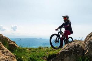 Side view of male tourist relaxing on top of hill enjoying beautiful mountain scenery wearing helmet covering his whole face. Active extreme recreation concept photo