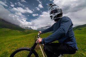 Back view wide angle of mountain bike and man in mountains against mountain range and hills with clouds and blue sky. Extreme sports concept, relaxation during training photo