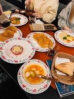 People are sharing a meal of potato pancakes, soup, salad, and bread, served on decorative plates and bowls in a cozy restaurant setting, highlighting the rich culinary traditions of Eastern Europe photo