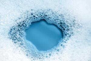 White soap foam. A frame of foam bubbles on a blue background with a place to copy text. The texture of soap bubbles in close-up. Bubble bath. Laundry gel. Soap for washing photo