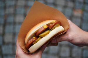 A close up of a hot dog with pickles and mustard in a paper wrapper. photo