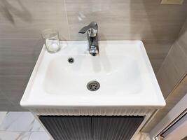 A sink with a silver faucet and a glass on the counter photo