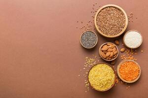 Various superfoods in smal bowl on colored background. Superfood as rice, chia, quinoa, lentils, nuts, sesame seeds, almonds photo