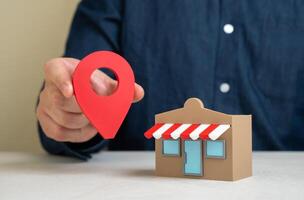 A man holds a geolocation pin near a store. Convenient location and high customer traffic. Business visibility. Role of location in boosting sales, branding, and competitive edge. photo