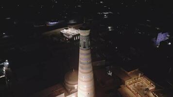 Minaret of Khiva illuminated by night with cityscape of Uzbekistan behind video