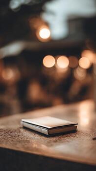 Closed Book on Table with Warm Bokeh Background. A detailed image of a closed book resting on a table, illuminated by warm, out of focus lights. photo