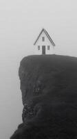 Solitary House on a Foggy Clifftop. A minimalist architectural scene of a small white house perched dramatically on a cliff edge, shrouded in mist. photo
