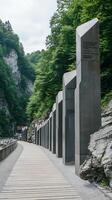 Modern Memorial Pathway in a Mountainous Green Landscape. A scenic walkway lined with tall, sleek monuments amidst lush greenery and rocky terrain. photo