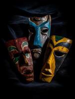 Three Hand Carved Wooden Masks on Dark Background. A close up image of three unique tribal masks, each with distinct colors and designs. photo