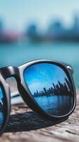 City Skyline Reflected in Sunglasses on Wooden Surface. A close up image showing a cityscape reflected in the lenses of sunglasses resting on wood. photo