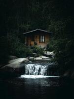 Secluded Log Cabin by a Waterfall in a Dark Forest. A tranquil scene of nature's beauty. photo