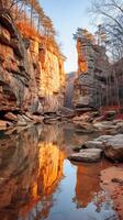 Serene Autumn Reflection in a Sandstone Gorge. Golden sunlight illuminates the cliffs and trees, perfectly mirrored in the tranquil water below. photo