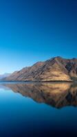 Mountain Reflection in a Calm Lake Under a Clear Blue Sky. A serene landscape photograph showcasing the perfect mirror image of a mountain range in still water. photo