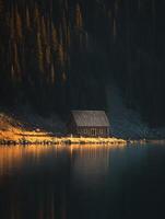 Secluded Lakeside Cabin at Golden Hour. A tranquil scene of a rustic wooden cabin nestled on the shore of a calm lake, bathed in the warm light of sunset. photo